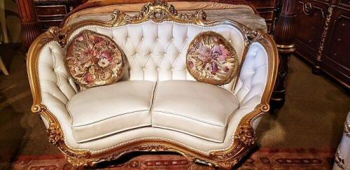 elegant carved wood french reproduction loveseat with ivory colored tufted cushion back and satin floral round pillows. Floor samples for sale.